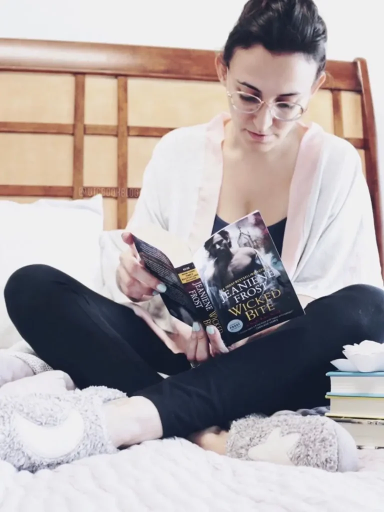 Francesca reading Wicked Bite by Jeaniene Frost, a Night Huntress World paranormal romance, curled up on a bed.