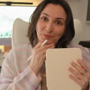 Francesca in a pastel striped cardigan holding an iPad mini in a cream case and an Apple Pencil, making a thoughtful face in her cozy office