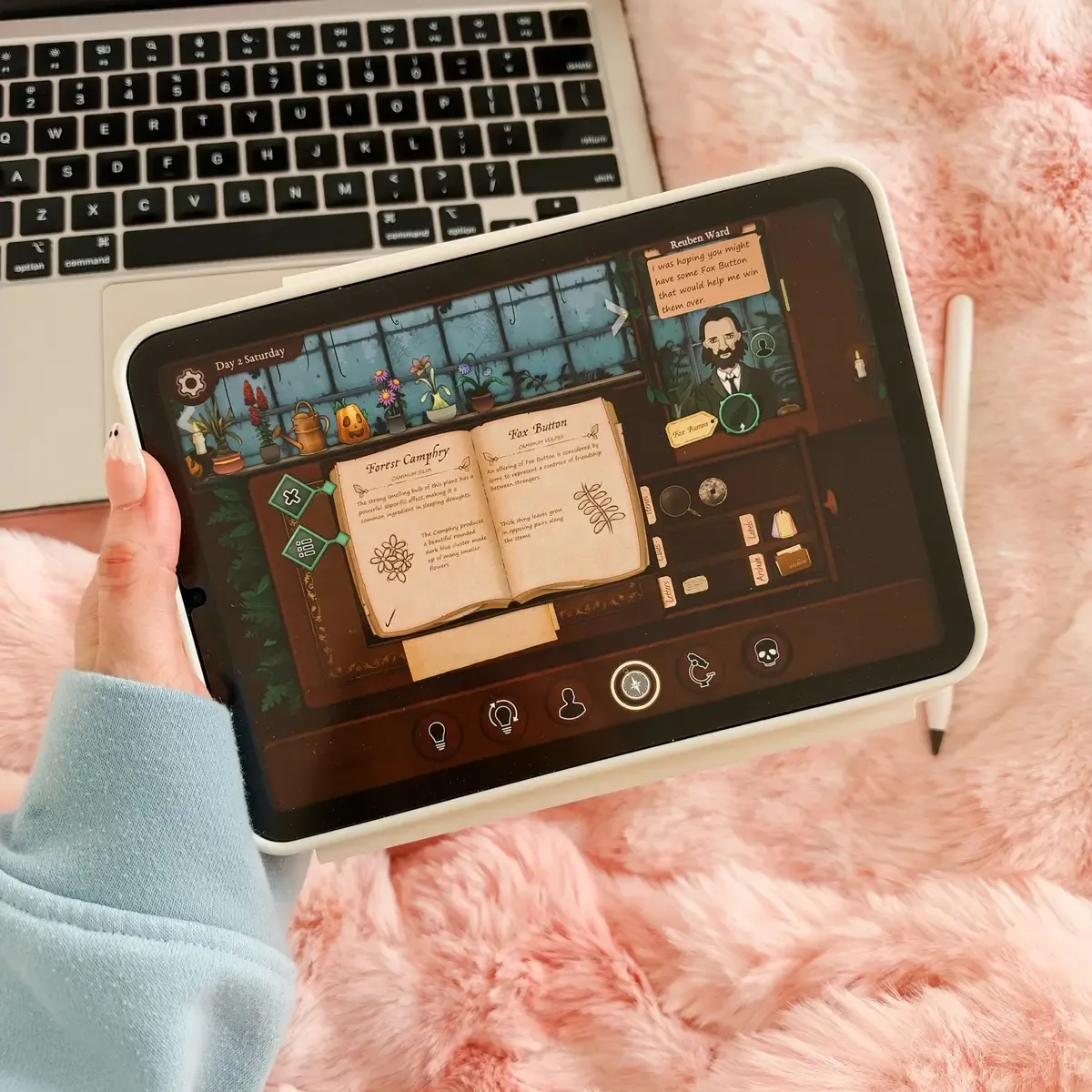 Holding an iPad playing Strange Horticulture on a pink faux fur throw, the plant encyclopedia open to Forest Camphry and Fox Button while a customer asks for a Fox Button, with a jack-o'-lantern on the shop shelf