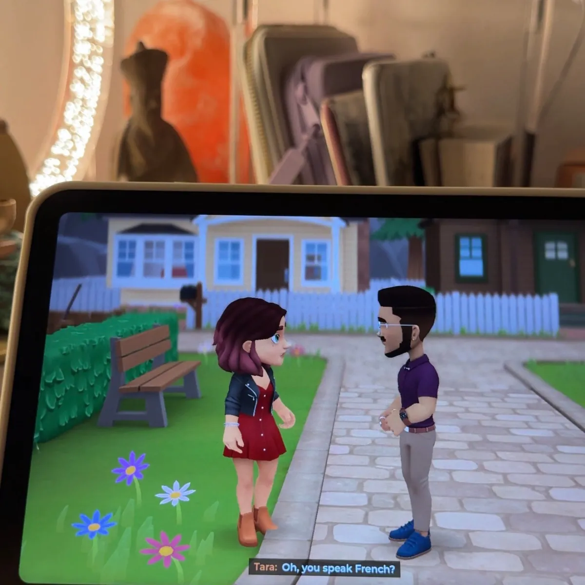 Wylde Flowers on an iPad, with Tara chatting to a townsperson on a garden path in front of a row of houses, the subtitle asking if he speaks French